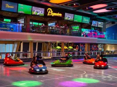 Auf der Odyssey of the Seas fahren mehrere Gäste farbige Bumper Cars. Über ihnen ist die Playmakers Sports Bar mit großen Bildschirmen zu sehen, die Sportübertragungen zeigen.