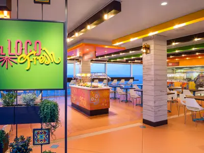 Innenansicht des farbenfrohen Restaurants "El Loco Fresh" auf der Odyssey of the Seas mit Buffettheke, Tischen, Stühlen und einem weiten Blick auf das Meer durch große Fenster.