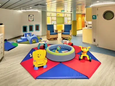 Blick in einen hellen, kinderfreundlichen Spielbereich an Bord der Odyssey of the Seas mit Matten, einer Ballgrube, Spielzeug und Schaukelstühlen.