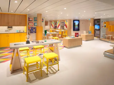 Innenansicht eines farbenfrohen Lernraums an Bord der Odyssey of the Seas mit gelben Schränken, Arbeitstischen und Hockern. Es sind Bücher, Laborgeräte und Bildschirme zu sehen.
