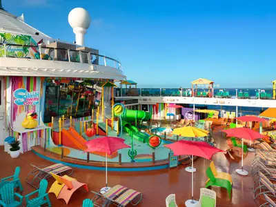 Kinder-Wasserpark „Splashaway Bay“ und Sonnendeck auf der Odyssey of the Seas mit Rutschen, Liegestühlen, Schirmen, Gummientchen, blauem Himmel und Meer.