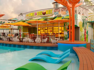 Blick auf die bunte Outdoor-Bar "The Lime & Coconut" und den Poolbereich der Odyssey of the Seas. Mit orangefarbenen Sonnenschirmen, Tischen, Stühlen und blauen Lounge-Liegen im Wasser.
