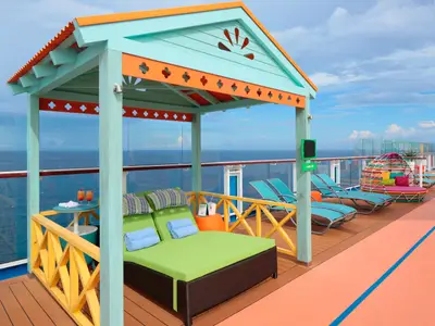 Blick auf das Sonnendeck der Odyssey of the Seas: Eine farbenfrohe Cabana mit Tagesbett und Cocktails, dazu weitere Liegen und ein buntes Rundbett vor weitem Meer.