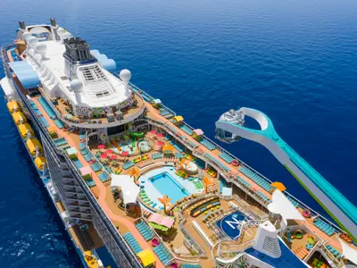 Die Odyssey of the Seas zeigt ihr sonniges Oberdeck mit Pools, Aqua Park, bunten Liegestühlen und der über dem Meer schwebenden Nordstern-Aussichtskapsel.