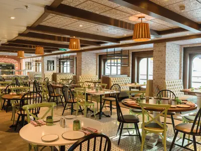 Das Restaurant der Odyssey of the Seas zeigt Tische, Stühle, Booth-Sitze, Backsteinwände, Fenster und Hängelampen. Im Hintergrund ein Pizzaofen.