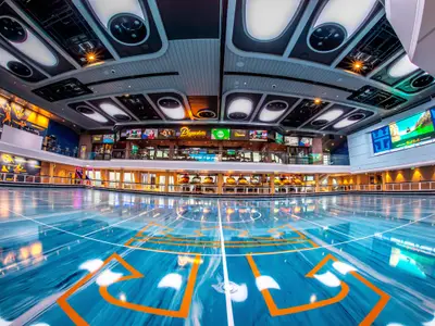 Das Sport- und Unterhaltungsdeck der Odyssey of the Seas mit blauem Spielfeld, "Playmakers" Sportsbar, vielen Bildschirmen und großer LED-Wand.