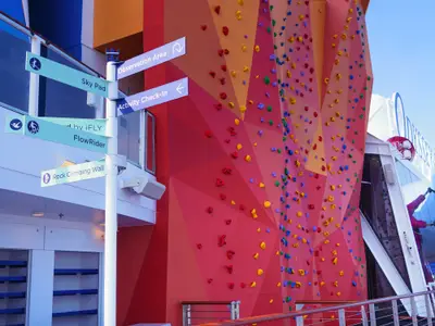 Nahaufnahme einer Kletterwand mit bunten Griffen und einem Wegweiser zu Aktivitäten an Bord der Odyssey of the Seas, wie iFLY und Sky Pad.