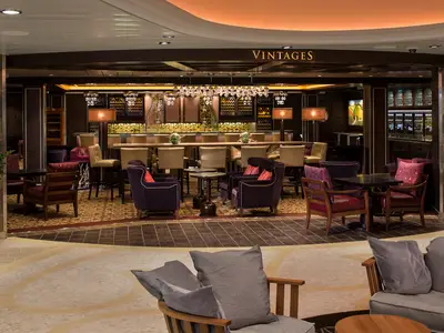 Die "Vintages" Weinbar auf der Ovation of the Seas. Elegante Lounge mit Barhockern, bequemen Sesseln, kleinen Tischen und dekorativer Beleuchtung. Warme Farbtöne dominieren das Interieur.