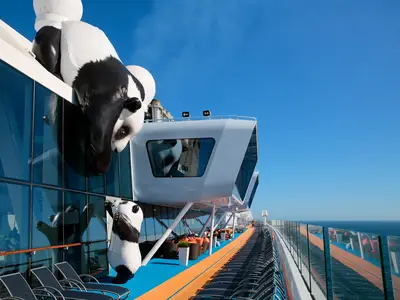 Die Ovation of the Seas zeigt große Panda-Skulpturen an Schiffswand und Deck, dazu die North Star Gondel, Liegestühle und das offene blaue Meer.