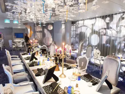 Innenansicht eines thematischen Restaurants mit langer, festlich gedeckter Tafel. Verschiedene Stühle, Kerzenleuchter und eine Decke mit schwebenden Objekten sind zu sehen. Eine Person ist im Hintergrund zu erkennen.