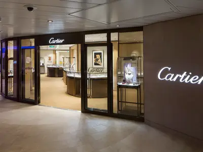 Cartier-Boutique auf der Ovation of the Seas. Der offene Eingang zeigt innen Schmuck und ein Leopardenbild. Leuchtende Logos an Wand und über der Tür.
