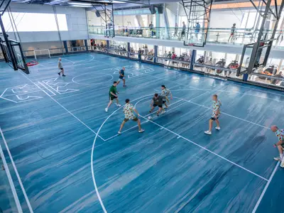 Auf dem Sportplatz der Ovation of the Seas spielen mehrere Männer Futsal. Die blau gemusterte Halle ist von verglasten Zuschauerdecks umgeben, auf denen weitere Personen stehen.