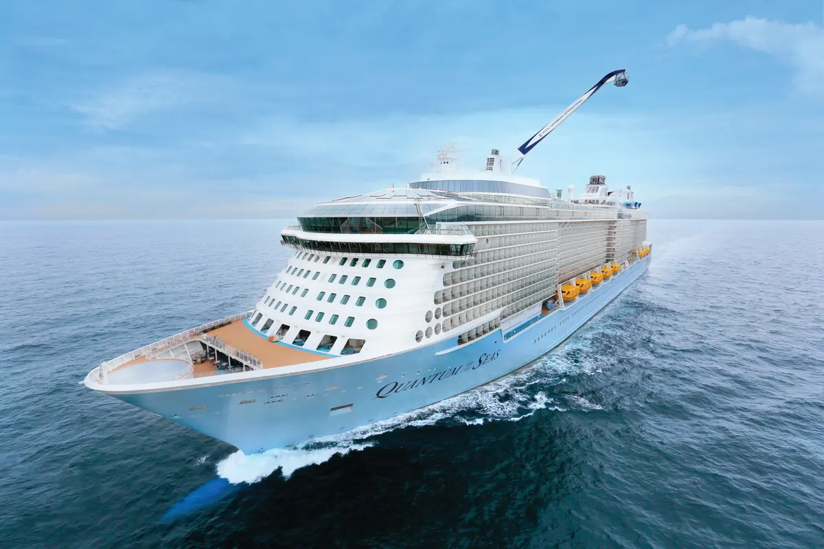 Die Quantum of the Seas, ein großes Schiff in Hellblau und Weiß, fährt auf offenem Meer. Am Bug schlagen Wellen, am Heck ist der gläserne Nord Star Arm zu sehen.