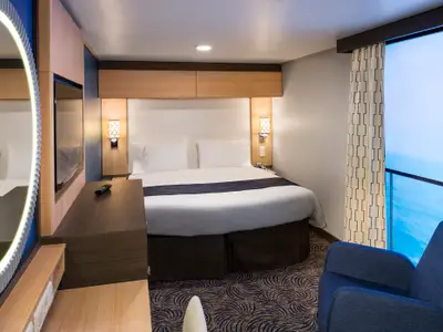 Einblick in eine moderne Innenkabine der Quantum of the Seas mit Doppelbett, TV, beleuchtetem Spiegel, Sessel und Meerblick.