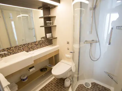 Ein modernes Badezimmer an Bord der Quantum of the Seas. Zu sehen sind Waschtisch, Spiegel, Toilette, Duschkabine und Badaccessoires. Fliesenboden in Braun- und Beigetönen.