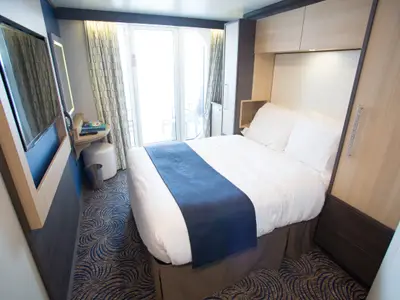 Blick in eine modern eingerichtete Balkonkabine der Quantum of the Seas mit Doppelbett, TV-Bereich und Balkonzugang.