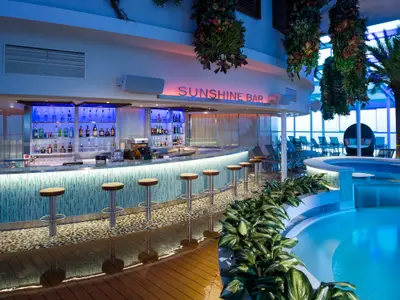 Die hell erleuchtete Sunshine Bar auf der Quantum of the Seas. Die blaue Bar mit Hockern und Schriftzug sowie ein blauer Poolbereich sind sichtbar.