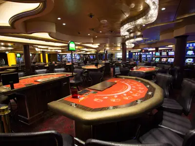 Das Foto zeigt das stilvolle Casino der Quantum of the Seas, mit mehreren leeren Spieltischen wie Blackjack und einer Reihe von beleuchteten Spielautomaten im Hintergrund.