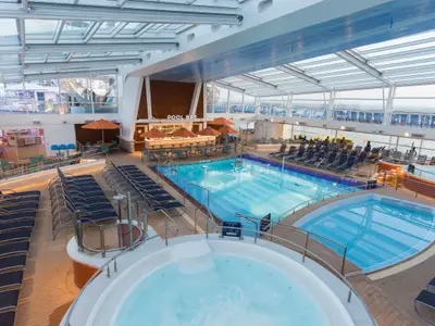 Überdachter Poolbereich der Quantum of the Seas mit Pools, Whirlpool, zahlreichen Liegestühlen und einer Poolbar unter Glasdach.