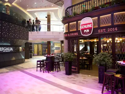 Detailansicht des Innenbereichs der Quantum of the Seas, mit Michael's Genuine Pub, Juwelier Regalia und Passagieren auf einer oberen Ebene.