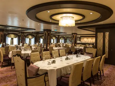Das elegante Restaurant der Quantum of the Seas ist mit vielen gedeckten Tischen und hellen Stühlen ausgestattet. Ein großer Kronleuchter und ein gemusterter Teppich prägen den Raum.