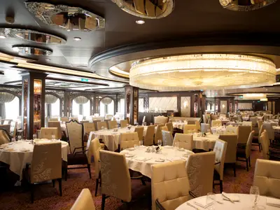 Das stilvolle Hauptrestaurant der Quantum of the Seas. Viele gedeckte Rundtische und elegante Stühle unter einem imposanten Kronleuchter und Spiegeldach. Eine luxuriöse Einrichtung für die Gäste an Bord.