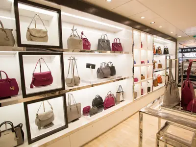 Helle Boutique an Bord der Quantum of the Seas mit Michael Kors Handtaschen und Accessoires in beleuchteten Regalen. Im Hintergrund ist eine Estée Lauder Auslage zu sehen.