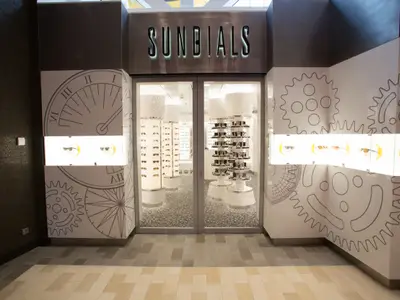 Eingang des Sonnenbrillengeschäfts 'SUNDIALS' auf der Quantum of the Seas. Die Fassade ist mit Sonnenuhren und Zahnrädern gestaltet. Sonnenbrillen sind innen und in Vitrinen ausgestellt.