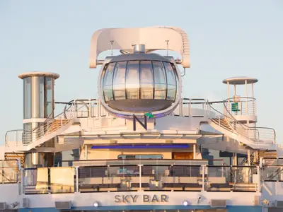 Das Oberdeck der Quantum of the Seas bei Sonnenlicht, mit der markanten North Star Glaskapsel, geschwungenen Treppen und einer Außenterrasse der "SKY BAR".