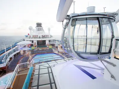 Die North Star Beobachtungsgondel ist über dem Pooldeck der Quantum of the Seas platziert, das auch Liegestühle und einen Whirlpool umfasst. Im Hintergrund ist das Meer sichtbar.