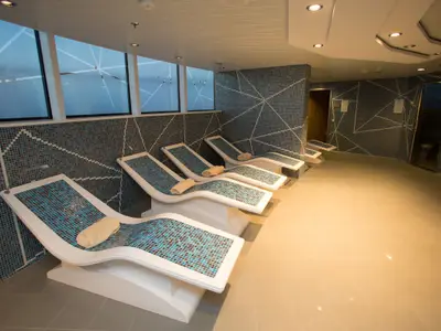 Blick in eine Thermal Suite an Bord der Quantum of the Seas. Mehrere Mosaikliegen mit Handtüchern stehen vor einer Fensterfront und gemusterten Wänden.
