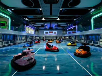 Bunte Bumper Cars auf glänzend blauem Sportboden der Quantum of the Seas. Digitale Anzeigetafel (12:10) und moderne LED-Beleuchtung prägen die Halle.