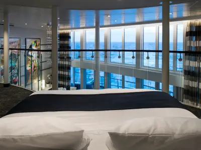 Obere Ebene einer Loft-Kabine der Quantum of the Seas. Im Vordergrund ein Bett, dahinter Glasgeländer. Große Fensterfronten bieten einen weiten Blick auf das offene Meer.