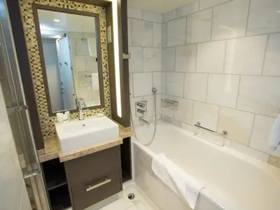 Innenansicht eines modernen Badezimmers an Bord der Quantum of the Seas. Zu sehen sind ein Waschtisch mit Spiegel, eine Badewanne mit Dusche und helle Wandfliesen.