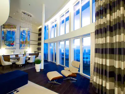Blick in eine luxuriöse, zweistöckige Suite auf der Quantum of the Seas mit raumhohen Fenstern, Essbereich, Kunstwerken und Lounge-Möbeln mit Meerblick.