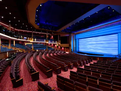 Das leere Haupttheater der Quantum of the Seas. Die Bühne mit blauem Bildschirm ist zentral. Lila und blaue Sitzreihen füllen den Raum, umgeben von dezenter Beleuchtung.