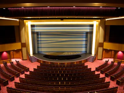 Das leere Haupttheater der Quantum of the Seas, von oben aufgenommen. Sichtbar sind geschwungene Sitzreihen, roter Teppich und eine beleuchtete Bühne mit Wellenmuster-Vorhang.