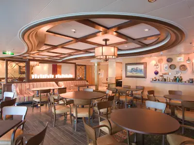 Innenansicht eines leeren Restaurantbereichs auf der Radiance of the Seas. Tische, Stühle, abgedeckte Bänke, Holzbalkendecke, Deko an Wänden.
