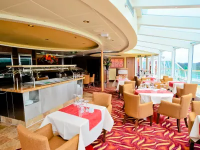 Buffetbereich und Restaurant auf der Radiance of the Seas. Gedeckte Tische, beigefarbene Stühle und große Fenster mit Meerblick sind zu sehen.