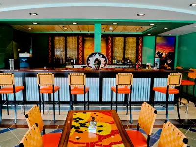 Blick auf einen bunten Barbereich an Bord der Radiance of the Seas. Die Theke ist mit Flaschen bestückt und davor stehen orangefarbene Barhocker. Ein großer Sombrero dekoriert die Bar.