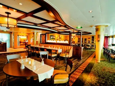 Ein Restaurant an Bord der Radiance of the Seas, mit Tischen, Stühlen und orange gestreiften Bänken. Warme Beleuchtung, Holzböden und Fensterfronten prägen den Raum.
