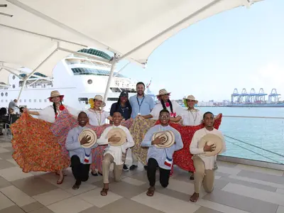 Eine Gruppe in traditioneller Kleidung posiert vor der Rhapsody of the Seas. Im Hintergrund sind Hafenkräne und ein Frachtschiff sichtbar.