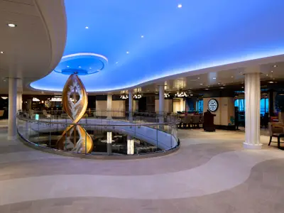 Atrium der Spectrum of the Seas: Goldene Skulptur, blaue Deckenbeleuchtung, Sitzbereiche und Restaurants, z.B. 'Jamie's Italian'.