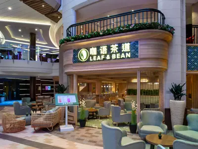 Das Bild zeigt das Café Leaf & Bean mit seinen Sitzbereichen im Atrium der Spectrum of the Seas. Mehrere Ebenen des Schiffs sind sichtbar, mit gemütlichen Möbeln und einem digitalen Menüstand davor.