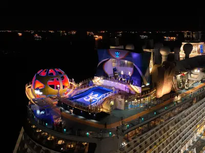 Obere Decks der Spectrum of the Seas bei Nacht. Hell beleuchtet sind North Star Kapsel, FlowRider Surfsimulator, iFLY Anlage und Kletterwand.