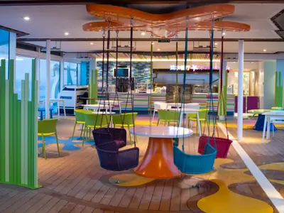 Ein farbenfrohes Café an Bord der Spectrum of the Seas. Man sieht Tische mit schwebenden Schaukelstühlen, leuchtend grüne Stühle, eine bunte Servicetheke und große Fenster.