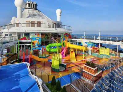 Der bunte Kinder-Wasserpark Splashaway Bay an Deck der Spectrum of the Seas. Man sieht Wasserrutschen, Spielstrukturen, Wasserfontänen, Liegestühle und das Meer unter blauem Himmel.