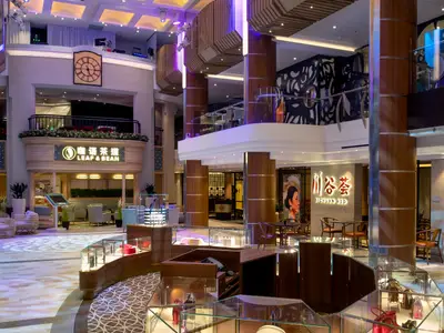 Innenansicht des Atriums auf der Spectrum of the Seas, mit Geschäften wie 'Leaf & Bean' und 'Sichuan Red' auf verschiedenen Ebenen. Im Vordergrund sind Auslagen zu sehen.