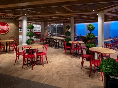 Innenansicht des Restaurants 'Sorrento's' an Bord der Spectrum of the Seas. Zu sehen sind viele Tische mit roten Stühlen, Holzfußboden und große Fenster mit blauem Meer im Hintergrund.