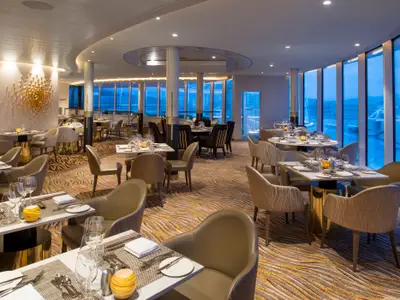 Das Restaurant der Spectrum of the Seas ist elegant eingerichtet. Es gibt viele gedeckte Tische, moderne Stühle und große Fenster mit Meerblick. Das Interieur ist in Beige- und Goldtönen gehalten.